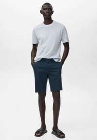 Light gray short-sleeve t-shirt, fitted design, paired with navy shorts and black sandals. Smooth texture, minimalistic style.