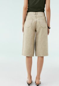 Beige denim Bermuda shorts med høj talje, bred snit og dobbelte baglommer, parret med en tætsiddende mørkegrøn top.