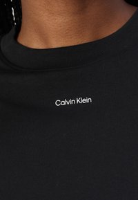 Sort bomulds T-shirt med rund hals. Har hvid broderet "Calvin Klein" logo placeret på venstre side af brystet.