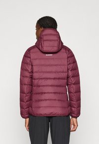 Μπορντό φουσκωτό μπουφάν με κουκούλα, με επεξεργασία καπιτονέ και διακριτικό λογότυπο στο άνω μέρος της πλάτης. Λείο υλικό και ελαστικές μανσέτες.