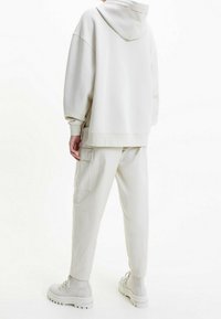 Sudadera gris clara con una gran capucha y puños acanalados, combinada con pantalones cargo a juego que tienen bolsillos laterales y botas de tobillo grises.