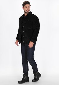 Fekete kordbársony dzseki, gallérral, patent gombokkal és hímzett részletekkel, sötét farmernadrággal és fekete fűzős csizmával párosítva.