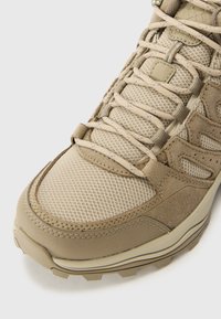 Chaussure de randonnée marron avec une tige en mesh, des superpositions en matériau synthétique et des accents texturés. Semelle extérieure en caoutchouc avec des crampons de traction pour une meilleure adhérence.