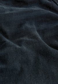 Temno modra denim tkanina z mehkimi teksturami, ki vsebuje subtilne tkanine in rahle odtenke, kar ustvarja bogato globino.