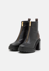 Zwarte leren enkellaarsjes met dubbele gouden ritsen, textuurbruin zijpanelen en chunky zwarte hakken met een gestructureerde zool.