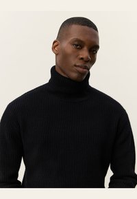 Schwarzer gerippter Rollkragenpullover, aus strukturiertem Strickmaterial gefertigt, mit hohem Kragen und taillierter Passform. Glatte Kanten und lange Ärmel.