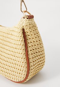 Sac à main beige crocheté avec garniture en cuir marron et fermoir en métal doré sur fond blanc uni.