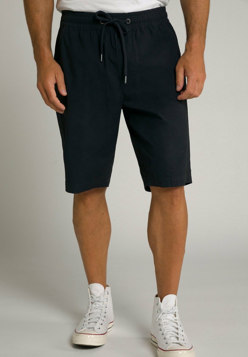 Dunkelmarineblaue Shorts aus weichem Stoff, mit einem Kordelzugbund und einem lässigen Schnitt, kombiniert mit weißen High-Top Sneakers.