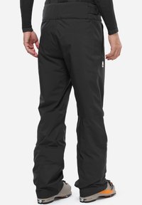 Schwarze wasserdichte Outdoor-Hosen mit geradem Bein, ausgestattet mit einer glatten Textur und einem Logo auf der Rückseite. Geeignet zum Skifahren.