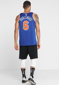 Blå baskettröja med orange detaljer och nummer 6, som bärs med svarta shorts, vita benärmar och mönstrade svarta strumpor.