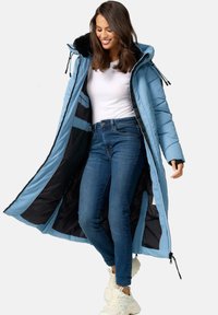 Lichtblauwe pufferjas met een bontgevoerd capuchon, ritssluiting en elastische manchetten. Draag het over een witte top en donkere jeans, met witte sneakers.