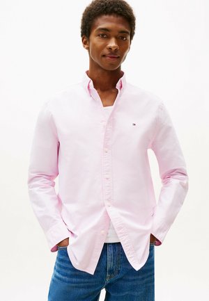 Helles rosa Baumwollhemd mit Knöpfen und Kragen, mit einem kleinen Logo auf der Brust, kombiniert mit blauen Jeans.