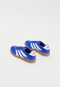 Un par de zapatillas Adidas Predator azules y blancas con suelas de goma, colocadas una al lado de la otra sobre un fondo blanco.