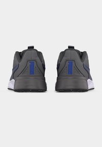 Ζευγάρι γκρι και μαύρα αθλητικά Puma με μπλε λογότυπο, από την πίσω όψη, που δείχνει επενδυμένη φτέρνα και λευκή ενδιάμεση σόλα.