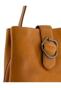 Sac en cuir tan avec une texture lisse, présentant un gros détail de boucle en argent sur une sangle et des coutures visibles le long des bords.