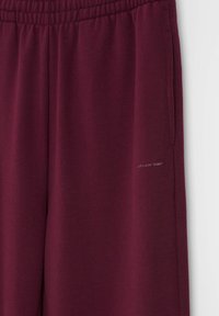 Burgundowe spodnie dresowe wykonane z miękkiego materiału, z elastycznym pasem, bocznymi kieszeniami i małym detalem logo na nogawce.