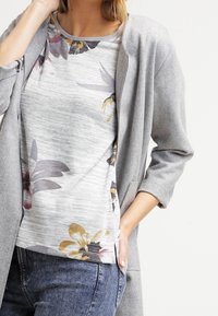 Cardigan grigio con maniche lunghe sopra un top grigio chiaro con motivi floreali in viola, giallo e nero. Tessuto testurizzato e vestibilità rilassata.