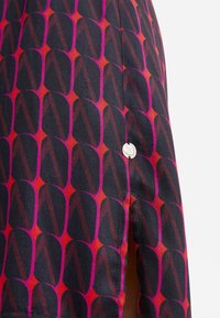 Spódnica w wzory z czarno-czerwono-różowym geometrycznym wzorem, z metalowym guzikiem w kolorze srebrnym i bocznym rozcięciem.