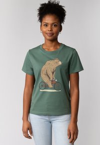 Groene katoenen t-shirt met een illustratie van een beer die op een rode fiets rijdt. Korte mouwen, ronde halslijn en een relaxte pasvorm.