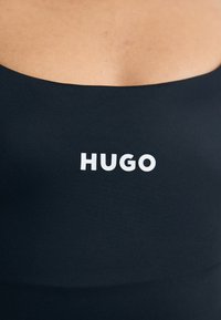 Námořnická modrá textilná tielko s okrúhlym výstrihom a bielym logom "HUGO" na strede. Tkanina vyzerá hladko a priliehavo.
