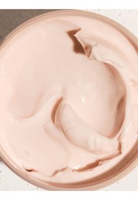 Glatter, hellrosa Creme mit glänzender Textur, teilweise verstrichen in einem runden Behälter mit einem natürlichen Holzdeckel.