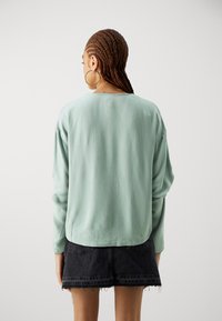 Mintgrønn langermet topp med teksturert stoff, løs passform og rund hals, parret med et svart denim miniskjørt.