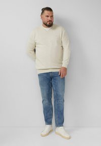 Beżowy sweter w serek z długimi rękawami, zestawiony z jasnoniebieskimi dżinsami i białymi trampkami. Gładka tekstura, swobodny krój i proste elementy designu.