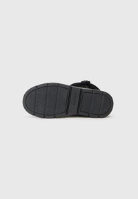 Čierna gumená podrážka sandálov s vystúpenými vzormi, vrátane kvetinových motívov a vlnkových línií, so zapuzdreným názvom značky "Skechers".