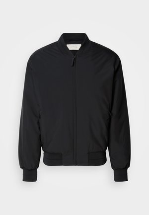 Črna bomberska jakna iz gladkega materiala, ki ima sprednji zadrgo, rebraste manšete in klasičen ovratnik. Minimalističen dizajn brez vzorcev.