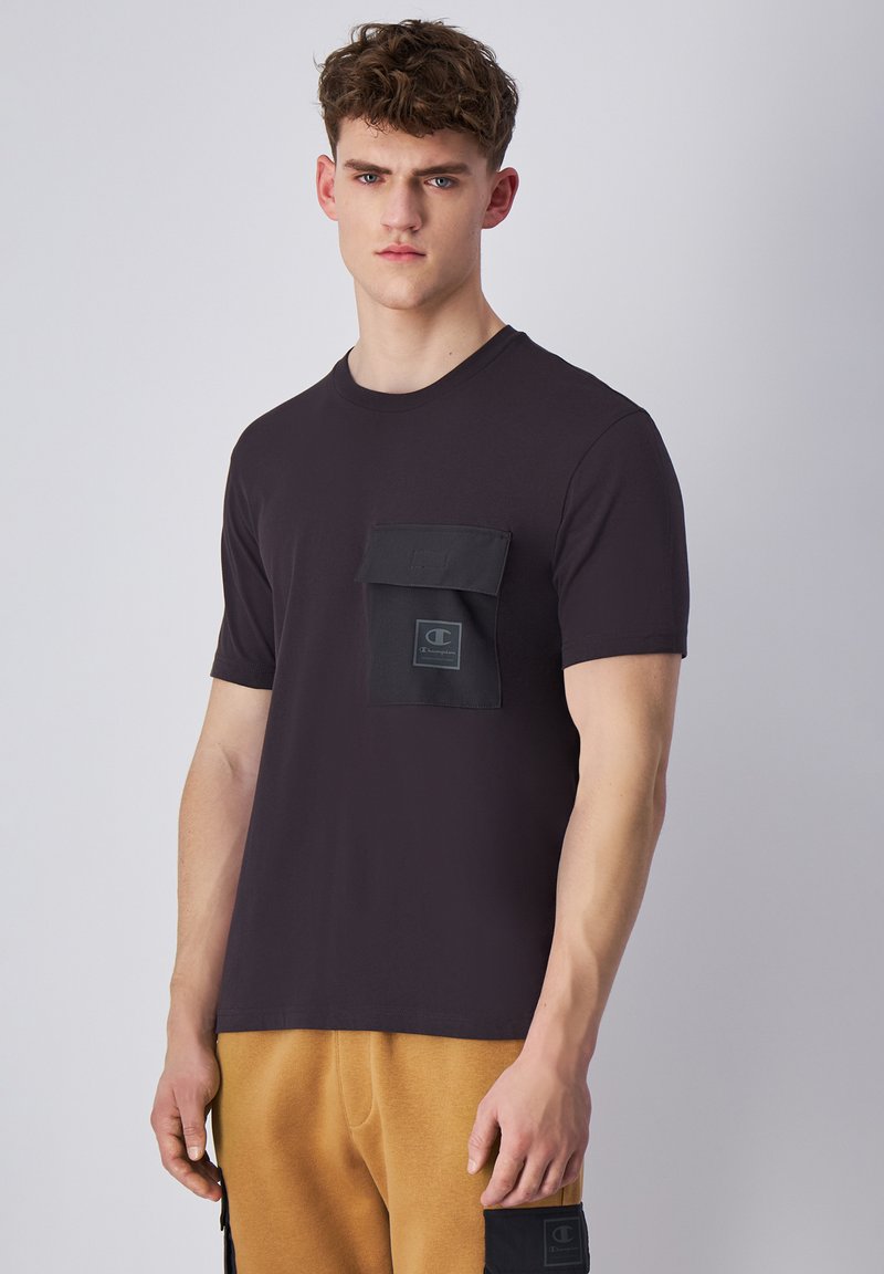 Camiseta de algodón negra con un bolsillo de parche cuadrado y detalle del logo en el pecho. Mangas cortas y escote redondo. Textura suave.