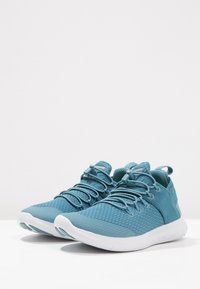 Světle modré sportovní boty s mesh svrškem, texturovaným designem, elastickými tkaničkami a bílou gumovou podešví. Výrazný poutko na patě pro snadné obouvání.