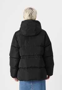 Juodas pūkinis švarkas su nuimamu kapišonu, su vertikaliu siuvimu, aptemptu liemeniu ir ilgomis rankovėmis. Lygus, blizgus paviršius.