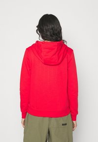 Sweat à capuche rouge avec une coupe décontractée, doté d'une poche kangourou, de poignets et d'un ourlet côtelés. Le matériau semble doux et texturé.