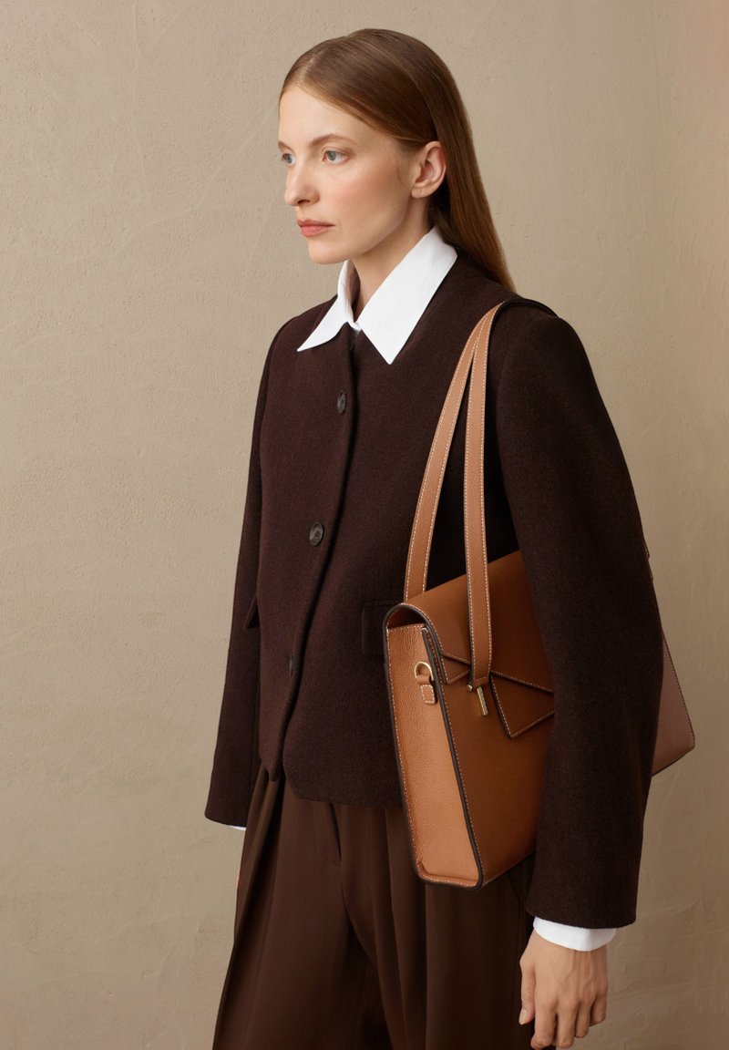 Giacca di lana marrone con colletto bianco e dettagli dei bottoni, abbinata a una borsa in pelle beige con patta e accenti di cucitura.