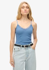 Blauw geribbeld tanktop met kanten rand langs de halslijn, gecombineerd met lichtblauwe high-waisted spijkerbroek en een zwarte riem.