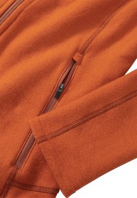 Orange Fleecejacke mit Seitentasche und gesteppten Akzenten. Strukturiertes Material mit glattem Reißverschlussdetail an der Vorderseite.