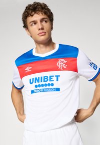Balts futbola krekls ar ziliem un sarkaniem akcentiem. Iekļauj V-veida kakla izgriezumu, īsas piedurknes un zīmolu "UNIBET" un "Zero% Mission". Izgatavots no gludas, vieglas materiāla.