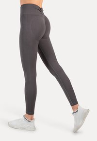 Legginsy z wysokim stanem w ciemnoszarym kolorze z teksturowanym wzorem, profilowanymi szwami i gładkim wykończeniem, zestawione z białymi butami sportowymi.