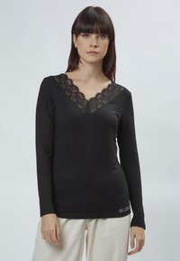 Schwarzes Langarmshirt mit einem Spitzen-V-Ausschnitt. Weicher Stoff, taillierte Form und das Wort "INFLUENCE" in einem metallischen Akzent am Saum.