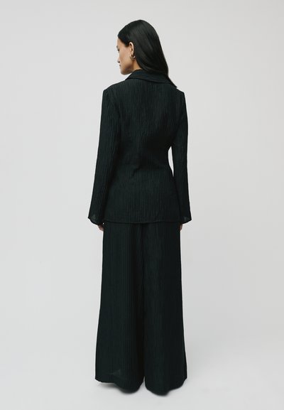 Black pinstripe suit with a tailored jacket and wide-leg trousers. Fabric has a textured finish, featuring a subtle sheen and sleek design.