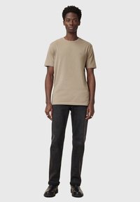 Beige cotton t-shirt with short sleeves and a round neckline, paired with dark gray jeans and black boots. Features a small logo on the chest.