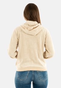 Felpa beige con cappuccio a coulisse, maniche raglan e polsini a costine. Tessuto morbido, dettagli di cucitura minimi e vita aderente.