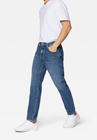 Vaqueros de mezclilla azul claro con corte recto, diseño de cinco bolsillos, acabado desgastado y cierre de botón, combinados con una camiseta blanca y zapatillas blancas.