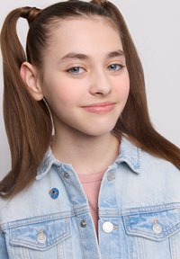 Jasnoniebieska kurtka dżinsowa z srebrnymi detalami, z niebieską i pomarańczową okrągłą przypinką po lewej stronie, noszona na różowej koszuli.