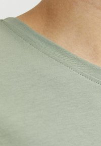 Světl zelené bavlněné tričko s designem V-výstřihu a jemným prošíváním kolem výstřihu a rukávů. Měkká textura s hladkým povrchem.