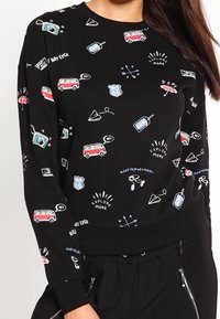 Sweatshirt noir avec des graphismes colorés sur le thème des voyages, comprenant des vans, des caméras et des boussoles ; présente un col rond et des poignets côtelés.
