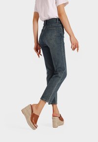 Jeans scuri a vita alta con taglio dritto e tasche posteriori, abbinati a sandali con zeppa marroni con dettaglio in paglia intrecciata.