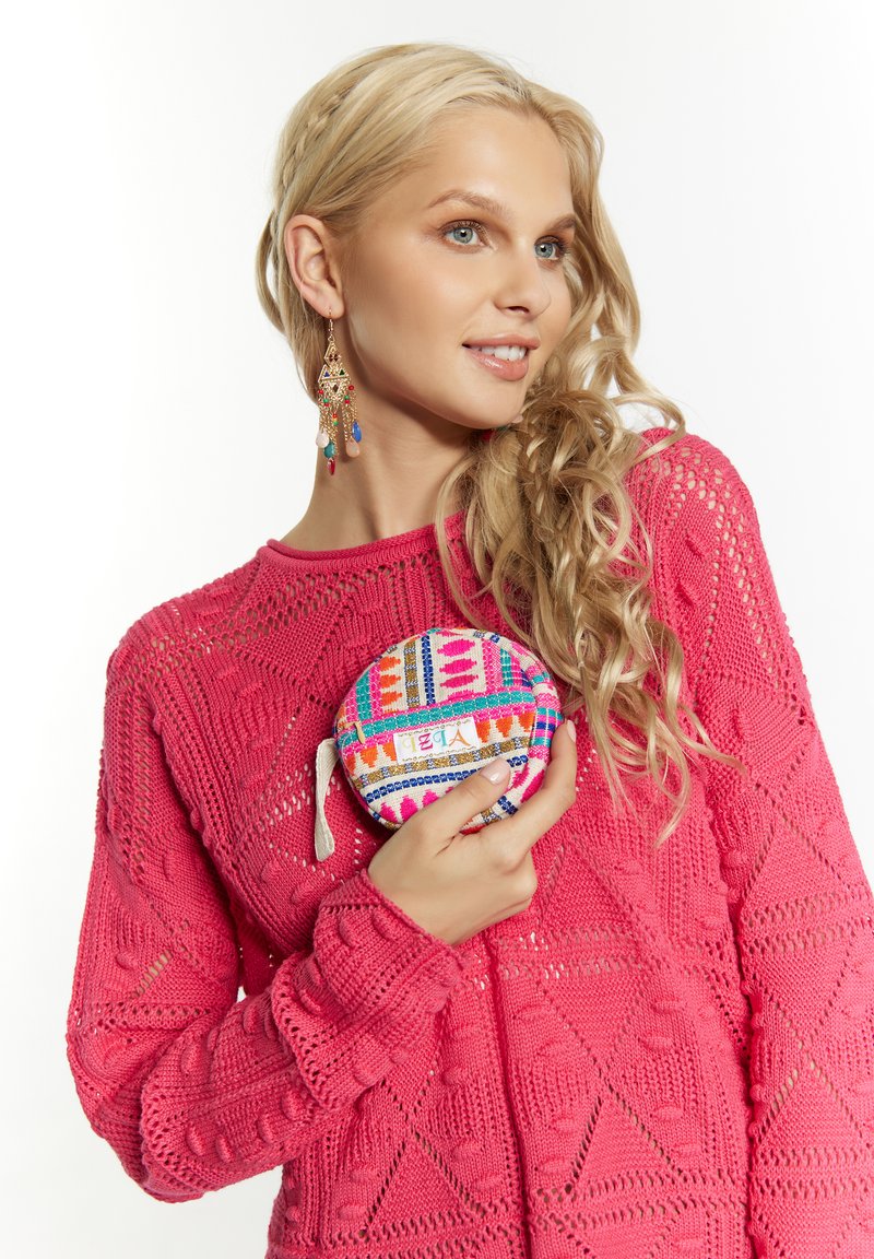 Ljusrosa stickad tröja med intrikata mönster; håller en cirkulär, flerfärgad påse med geometriska mönster och ett tag.