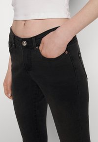 Melni džinsi ar šaurām kājām, ar gludu virsmu, ar priekšējiem kabatām un vara detaļām. Pieguļošs dizains vidukļa un gurnu rajonā.