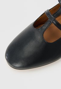 Black leather shoe with a rounded toe, featuring cut-out details and cross straps. Smooth texture with a matte finish.